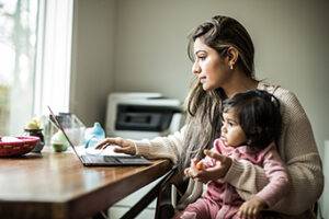 Mother multi-tasking with infant daughter in home office telehealth for kids