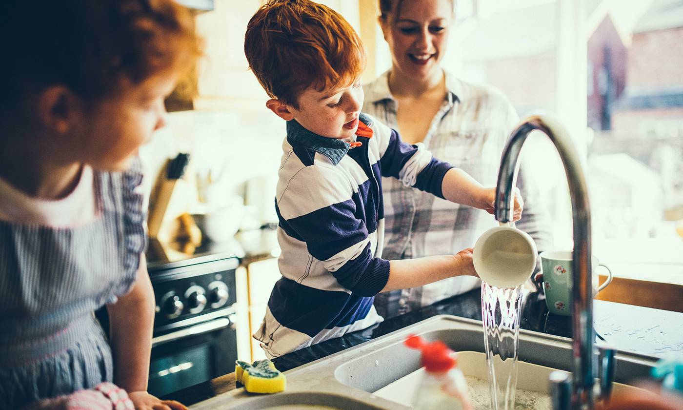 Two children and their Mother washing the dishes in the kitchen sink.-chores