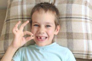 Lost milk-tooth, cute boy with long hair holding his tooth on thread