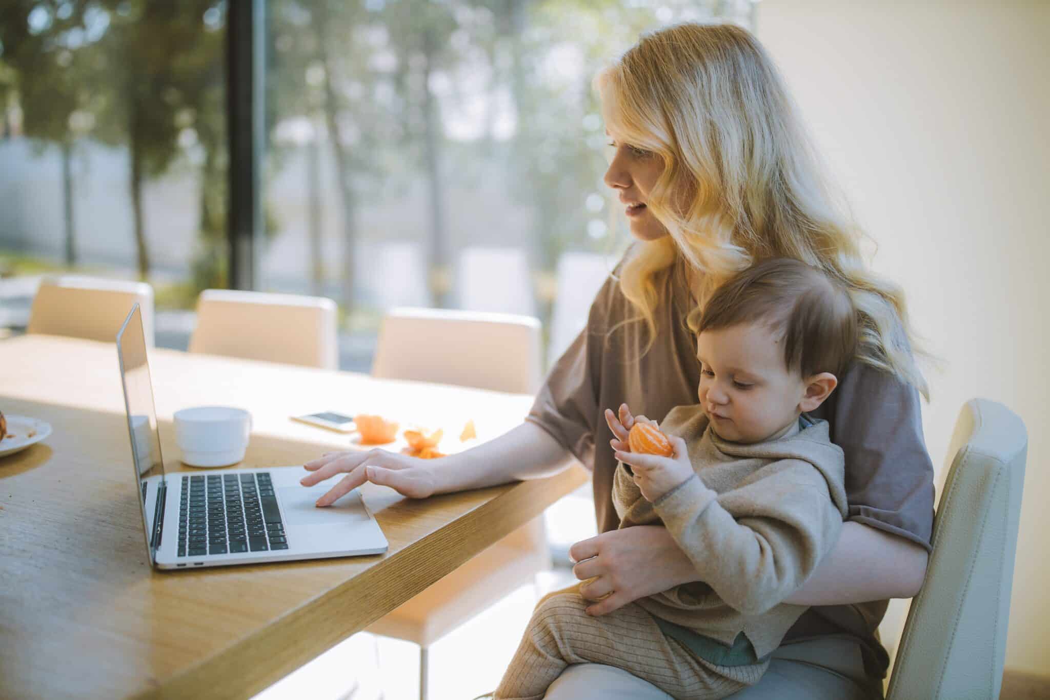 mom working while baby sitting on her lap eating orange -telemedicine